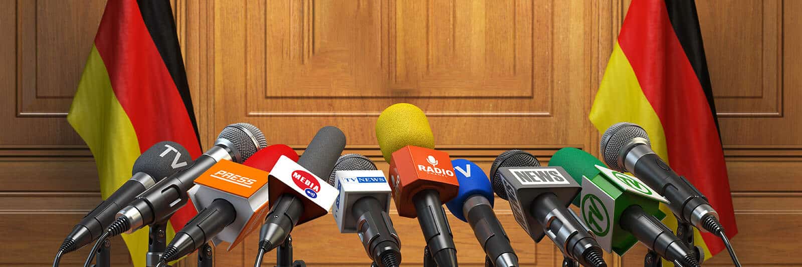 Multiple microphones set up for a press conference against a wooden backdrop.